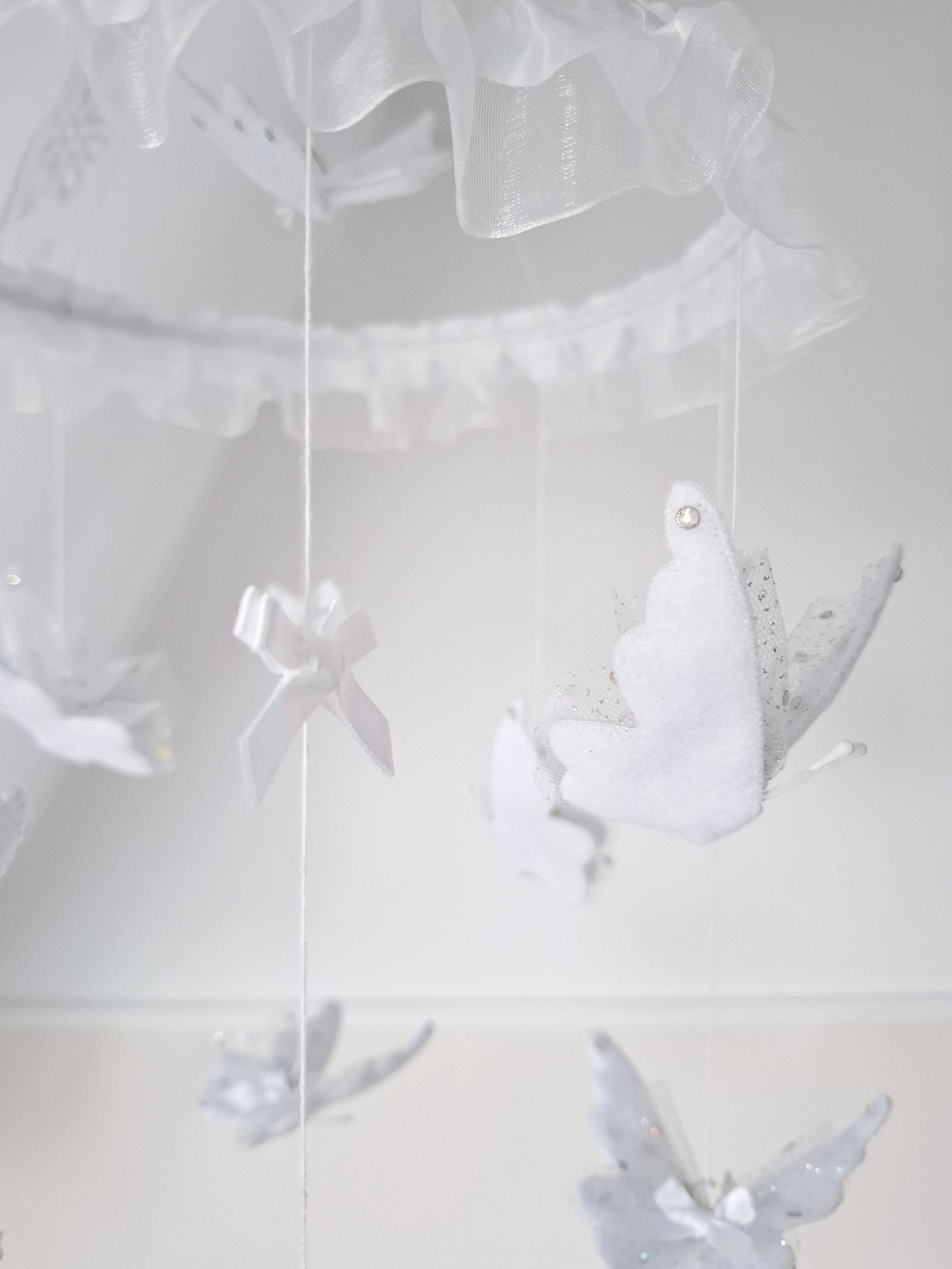 White-on-white baby mobile with soft butterflies and sheer ruffles, adding gentle elegance to a serene nursery design.