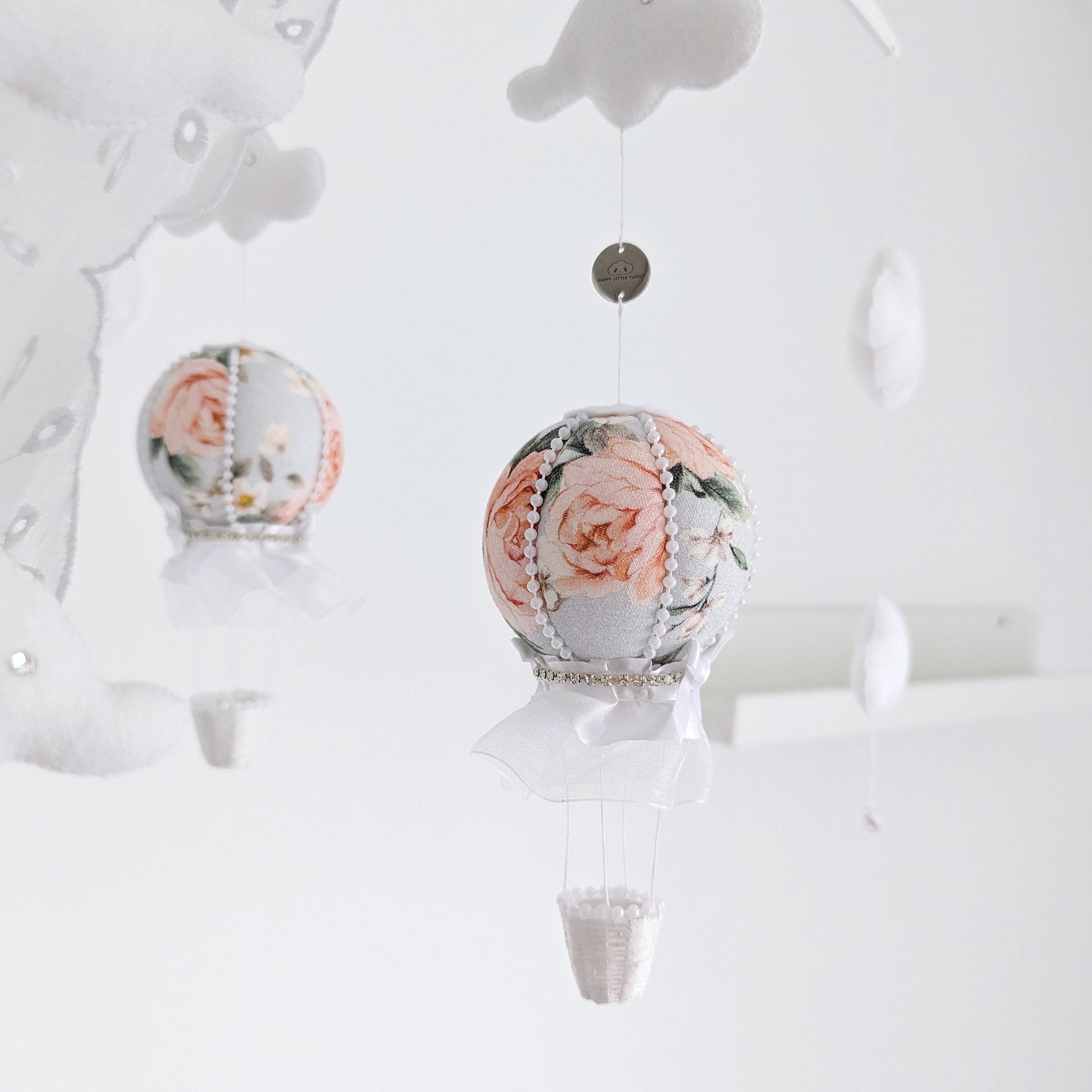 Side view of rose-print hot air balloons and white felt clouds on a handcrafted baby mobile.