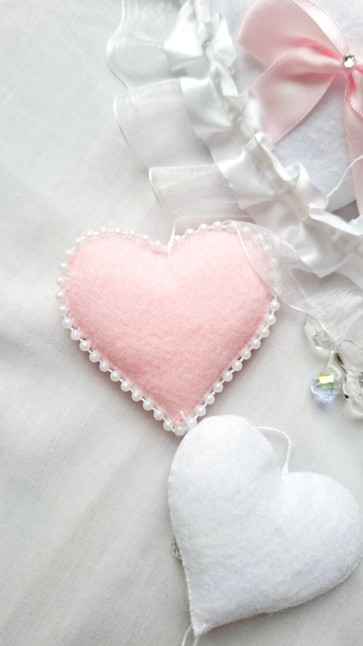 Flat lay of soft felt hearts in blush and white, gentle, handcrafted details from a luxury nursery mobile.