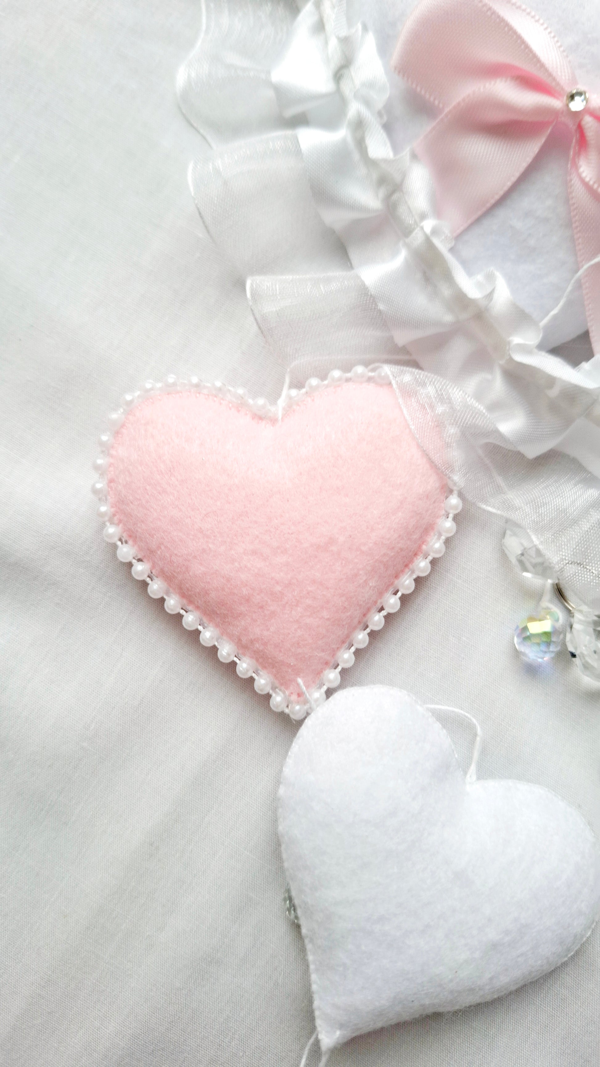 Flat lay of soft felt hearts in blush and white, gentle, handcrafted details from a luxury nursery mobile.