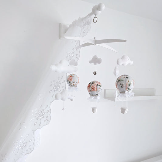 Delicate handmade baby mobile with floral hot air balloons, soft clouds, and a cross hanger in a white nursery.