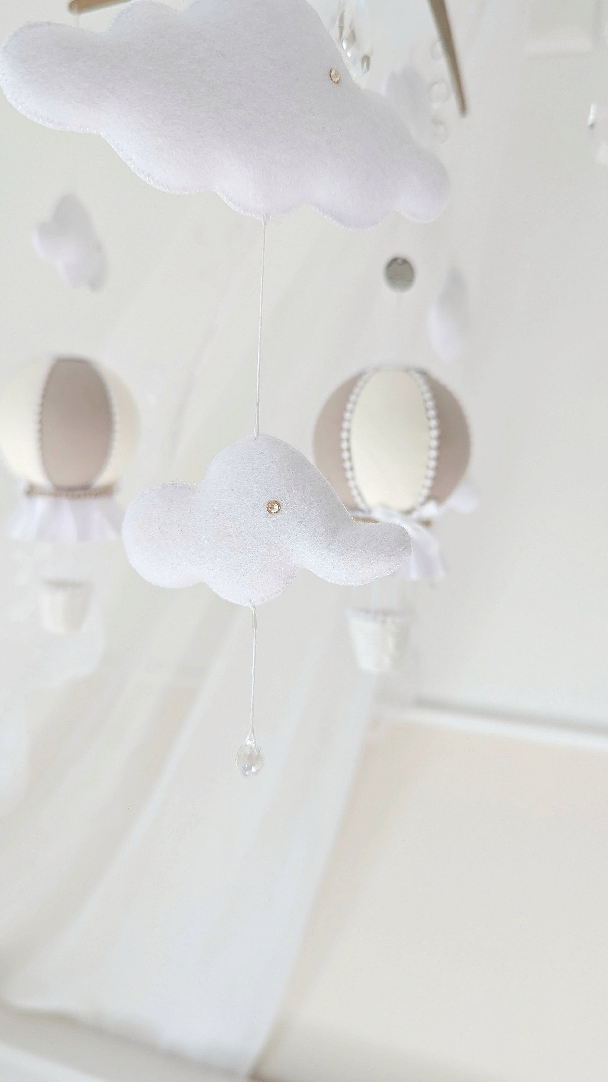 Handmade baby mobile with cloud and balloon elements, hung from a wooden cross frame with sparkling crystal accents.