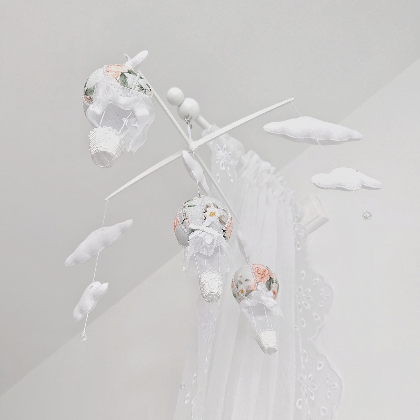 Soft-focus screen display of a floral hot air balloon baby mobile with clouds and cross hanger, viewed through a computer screen.