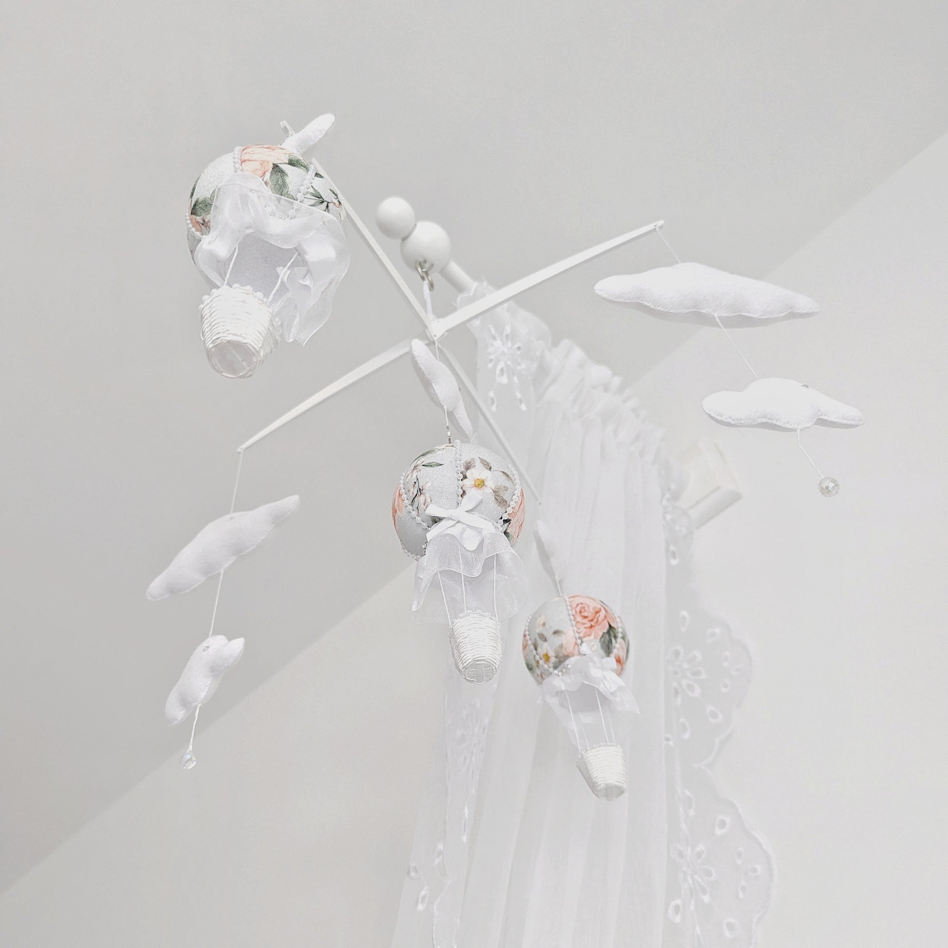Soft-focus screen display of a floral hot air balloon baby mobile with clouds and cross hanger, viewed through a computer screen.