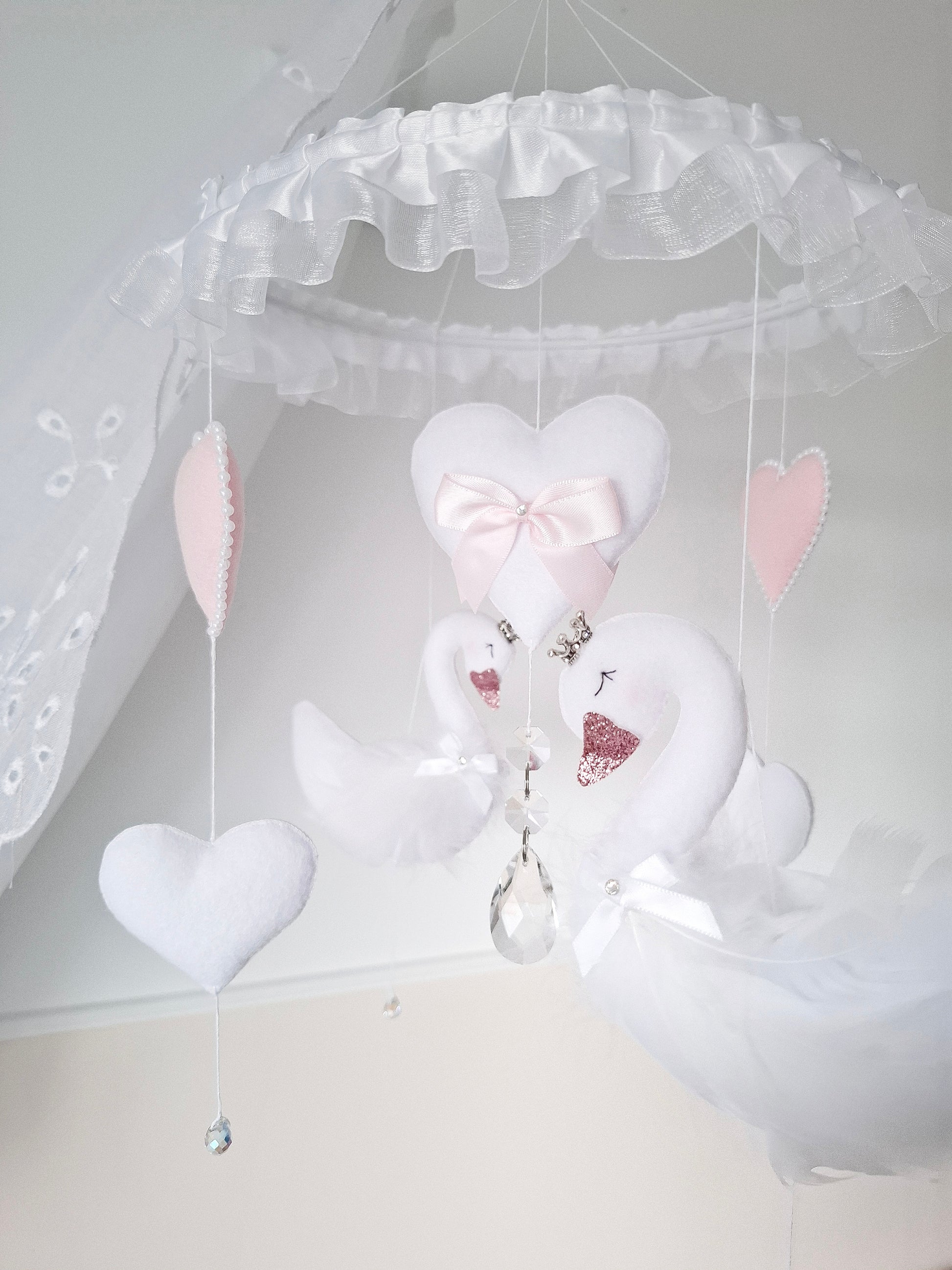 Side view of handmade swan baby mobile with hearts and crystals,elegant nursery decor in gentle pink and white.