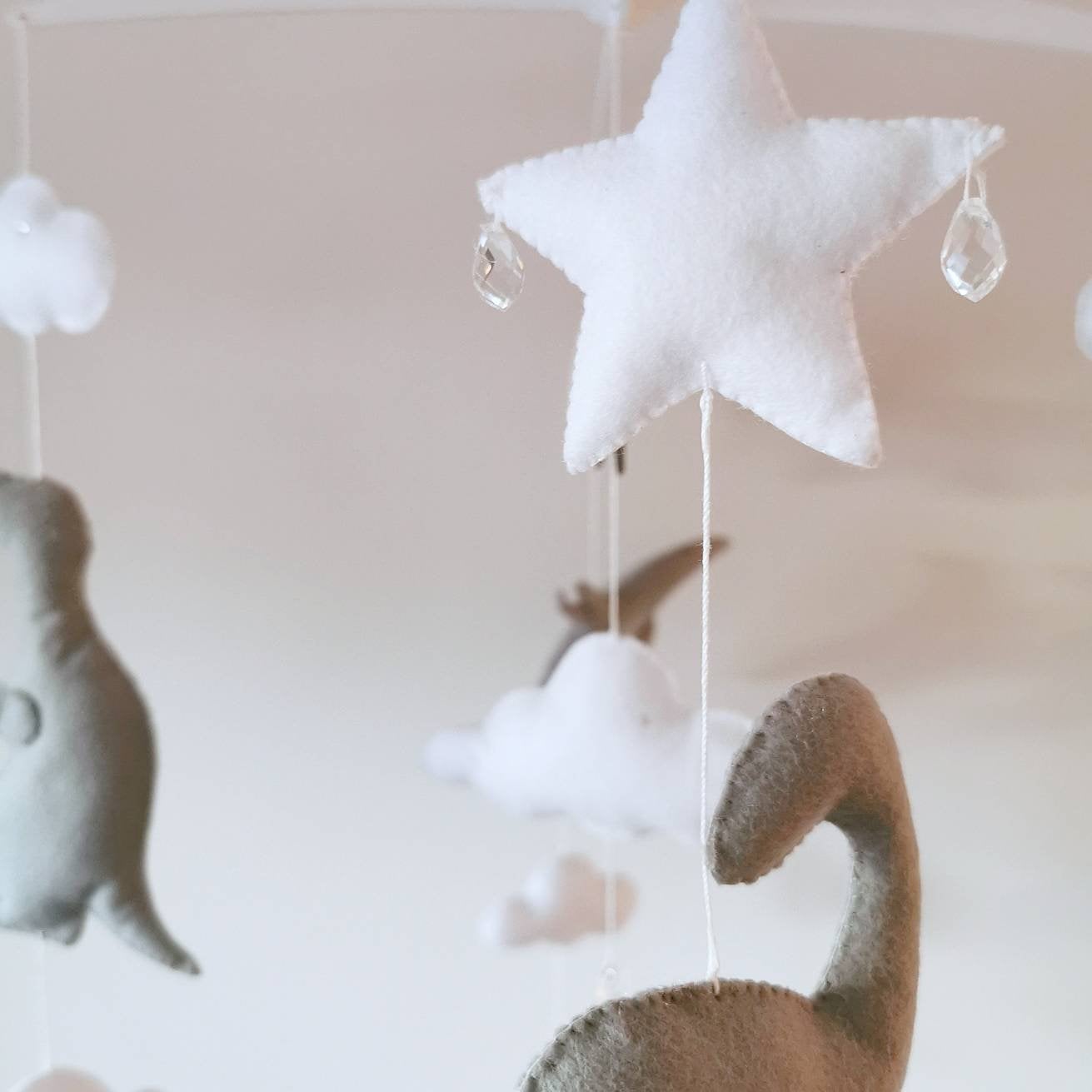 Playful nursery mobile featuring dinosaurs floating among stars and clouds in soft, neutral tones.