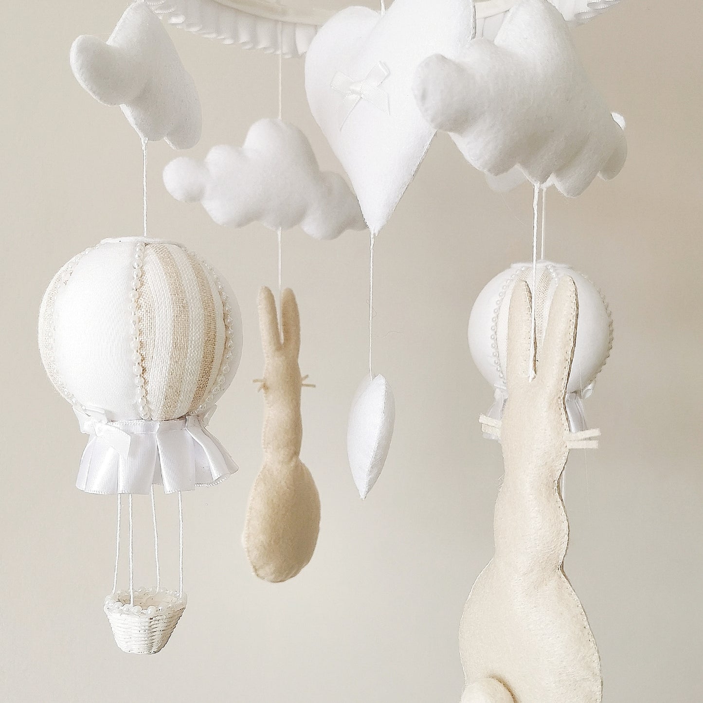 Handcrafted heirloom-quality baby mobile in warm cream tones with felt bunnies, balloons, and clouds.