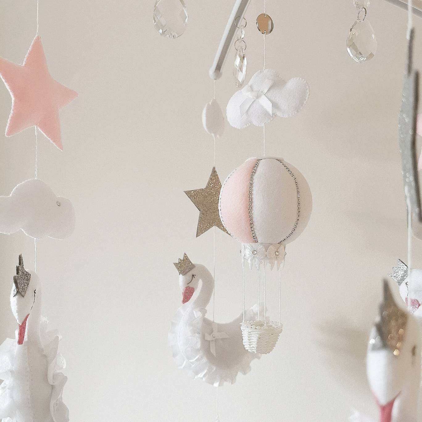 A close-up grouping of swans, stars and clouds made from soft felt in pink and white, highlighting the handmade beauty of each piece