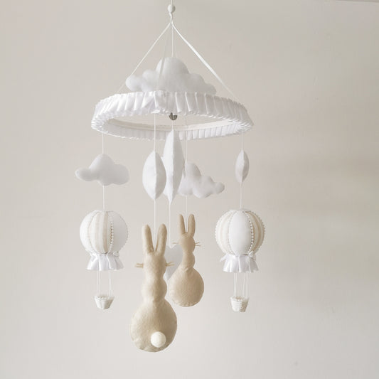 Soft neutral baby mobile with beige bunnies, white and striped beige balloons, and gentle clouds hanging from a round ruffled hanger.