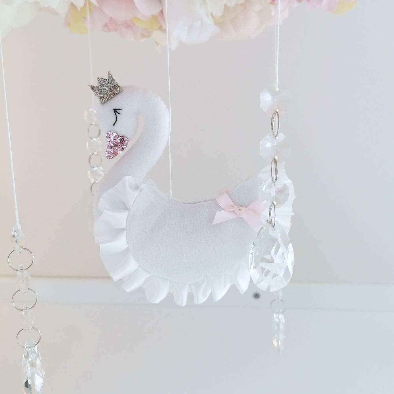 A gentle swan peeks out from a bed of pink and ivory flowers with crystals softly dancing below in this dreamy handmade nursery mobile
