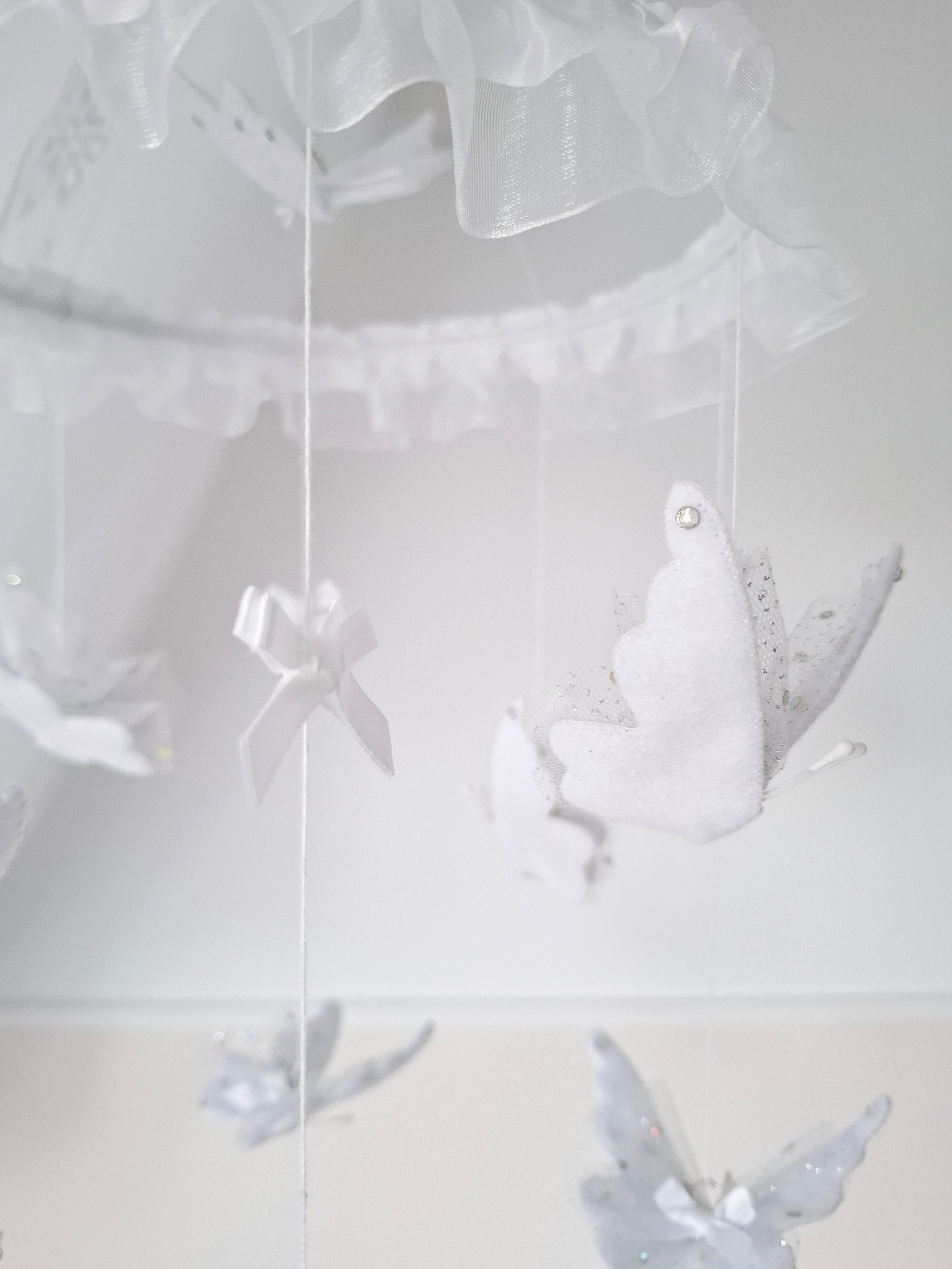 White-on-white baby mobile with soft butterflies and sheer ruffles, adding gentle elegance to a serene nursery design.

