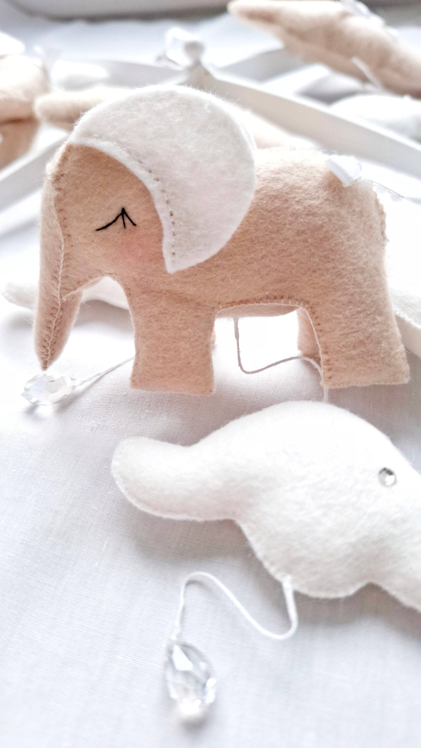 Detail view of felt elephant with embroidered ears and neutral tones, part of a handcrafted luxury mobile.