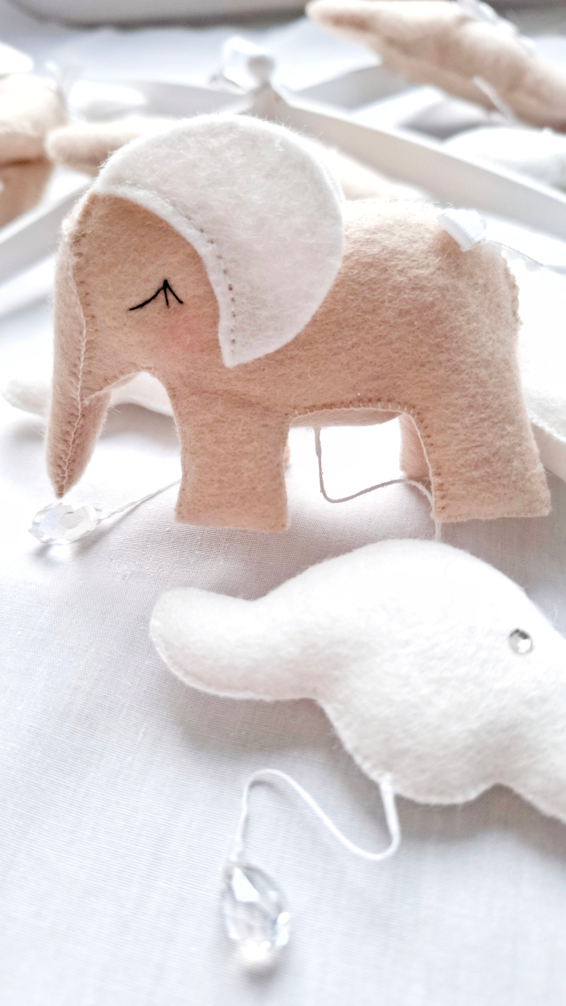 Detail view of felt elephant with embroidered ears and neutral tones, part of a handcrafted luxury mobile.
