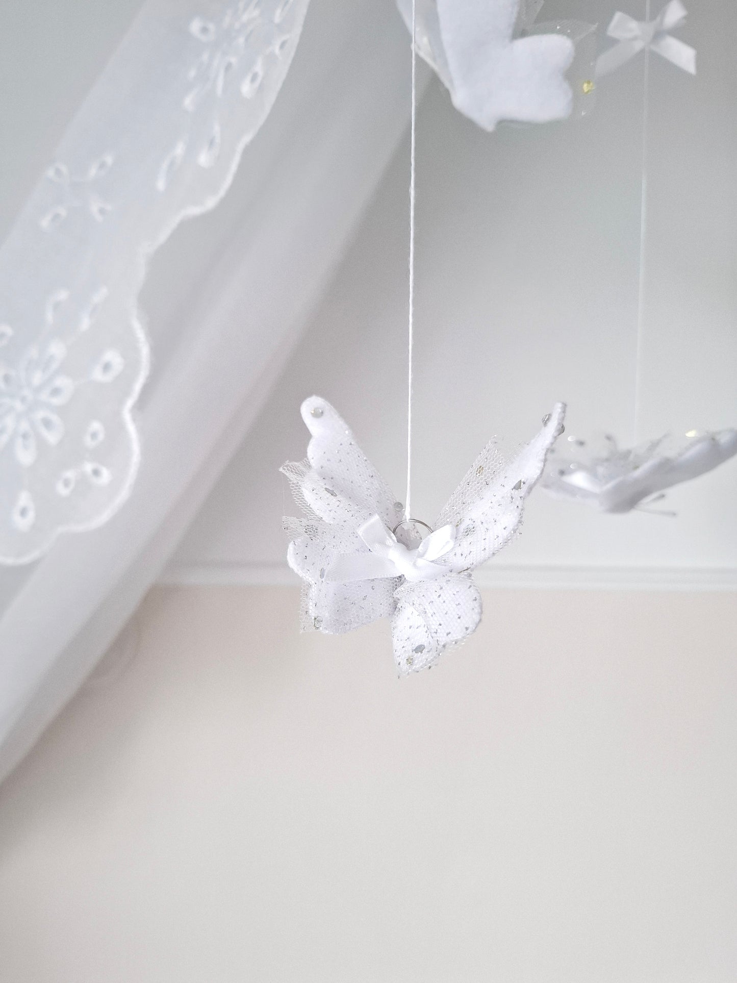 Handmade baby mobile with soft white butterflies and lace accents, designed to flutter gently above the crib in dreamy stillness.