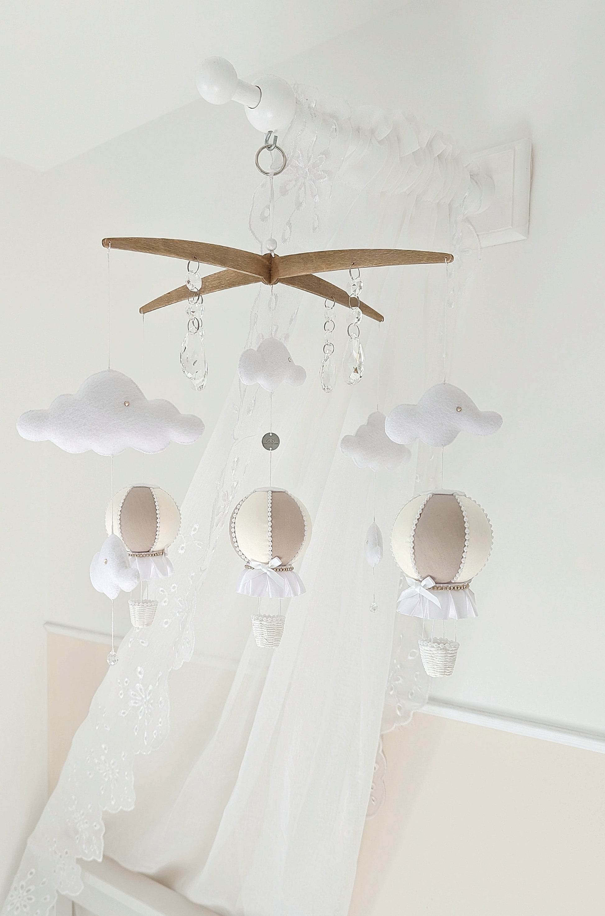 Luxury balloon mobile in soft neutrals with felt clouds and crystal drops, hanging above a pale nursery cot.
