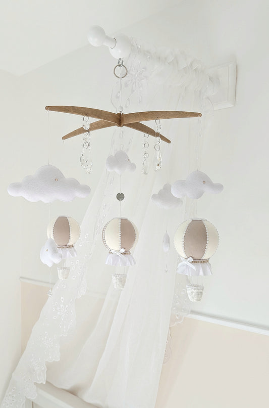 Luxury balloon mobile in soft neutrals with felt clouds and crystal drops, hanging above a pale nursery cot.