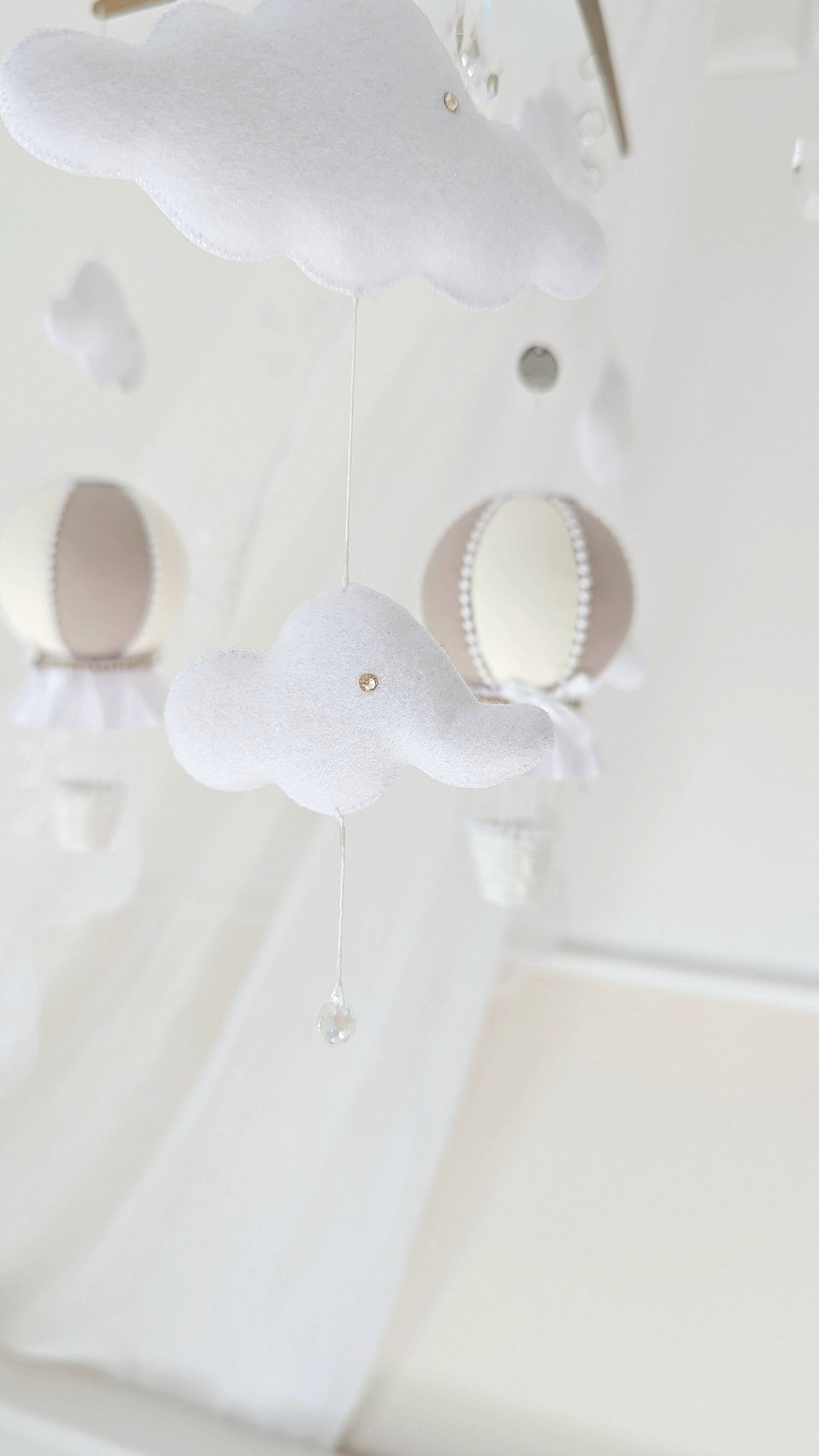 Handmade baby mobile with cloud and balloon elements, hung from a wooden cross frame with sparkling crystal accents.

