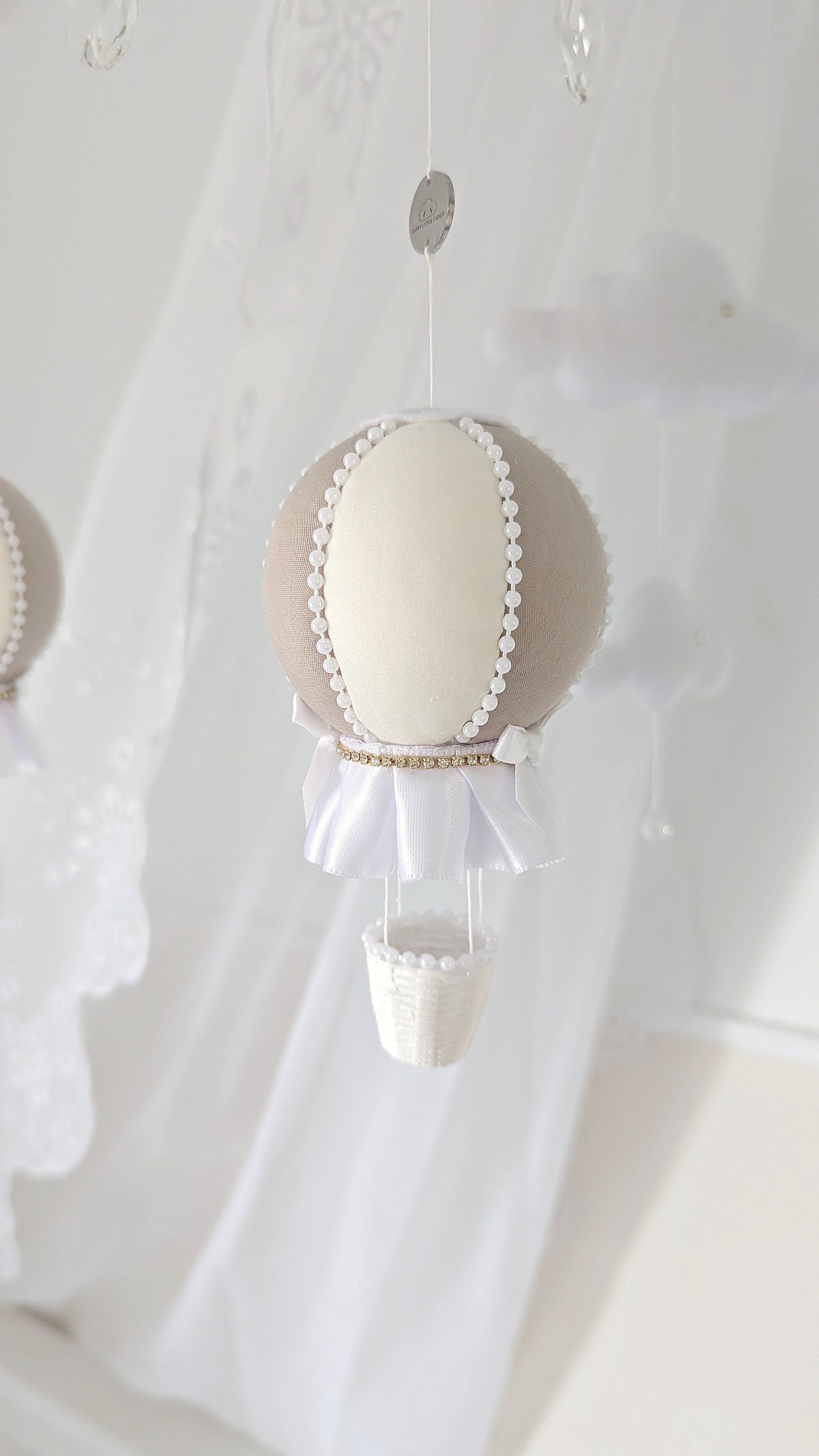 Close detail of a handmade balloon mobile in soft neutrals, with felt clouds, satin trim and a floating, gentle presence.


