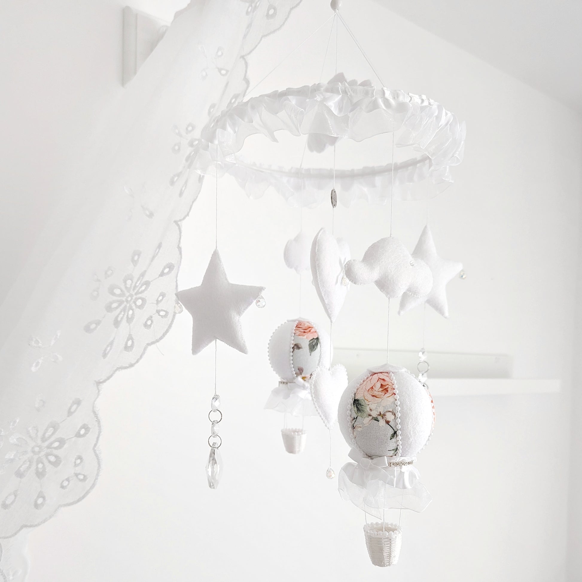 Dainty felt clouds, heart, and floral balloon on a handcrafted mobile designed for a soft, luxurious nursery.
