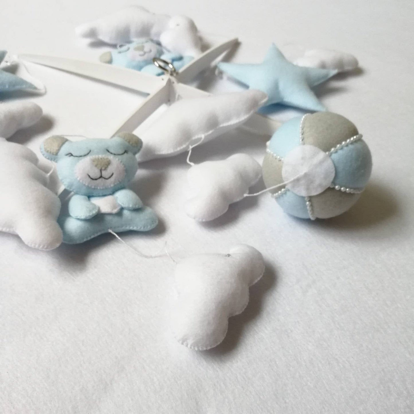 Flat lay of handmade baby mobile pieces in soft blue and white including clouds, stars, a balloon, and teddy.