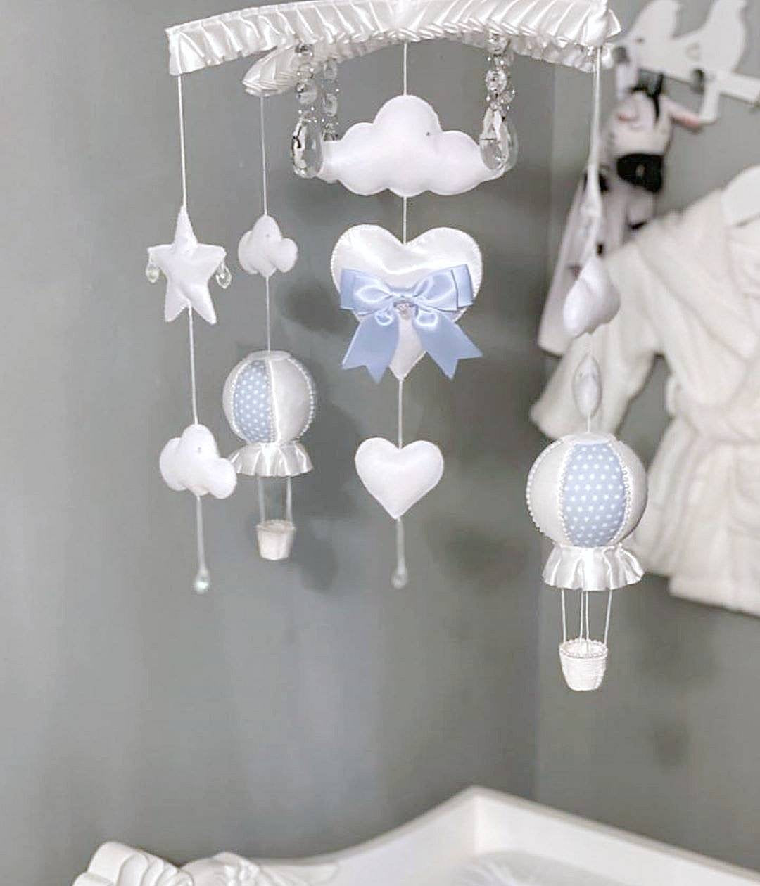Blue heart, hot air balloon and cloud baby mobile hanging above a crib in a softly lit nursery