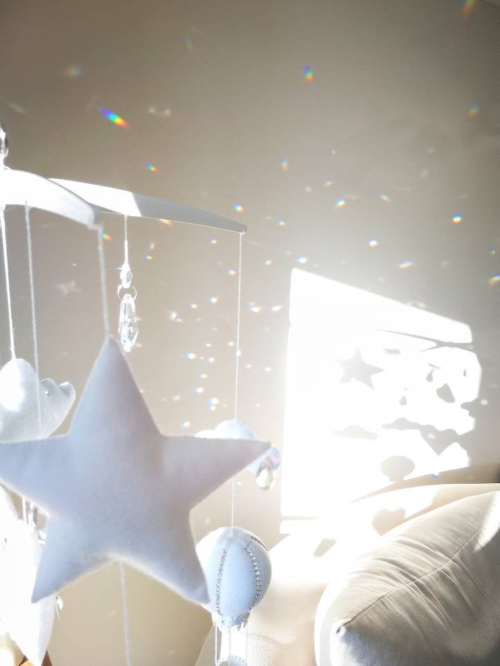 Detail of a felt star with soft white clouds and crustal sparkles in a dreamy nursery mobile setting.