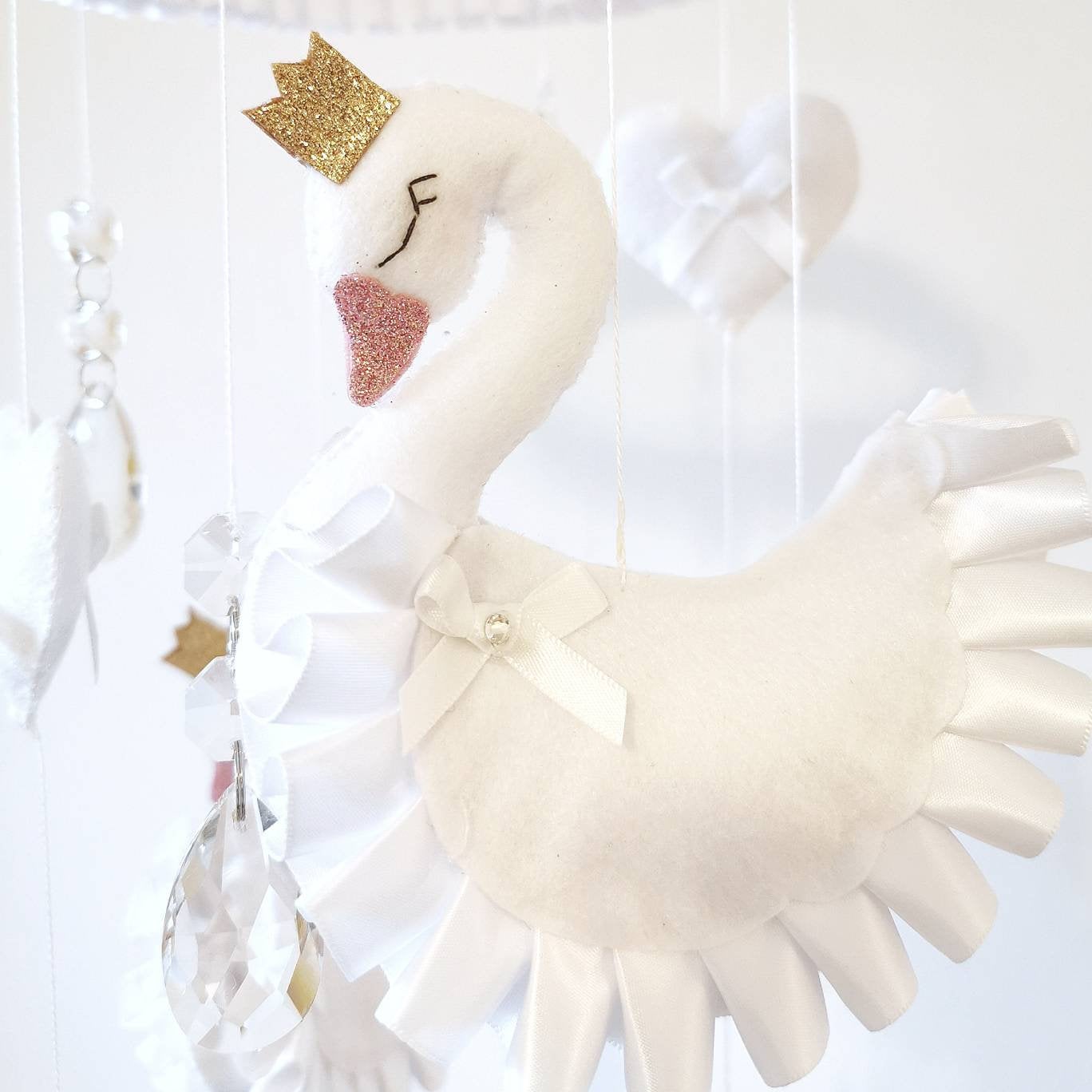 Dreamy nursery decor featuring a swan-themed baby mobile with frilly skirts and dainty crown details.