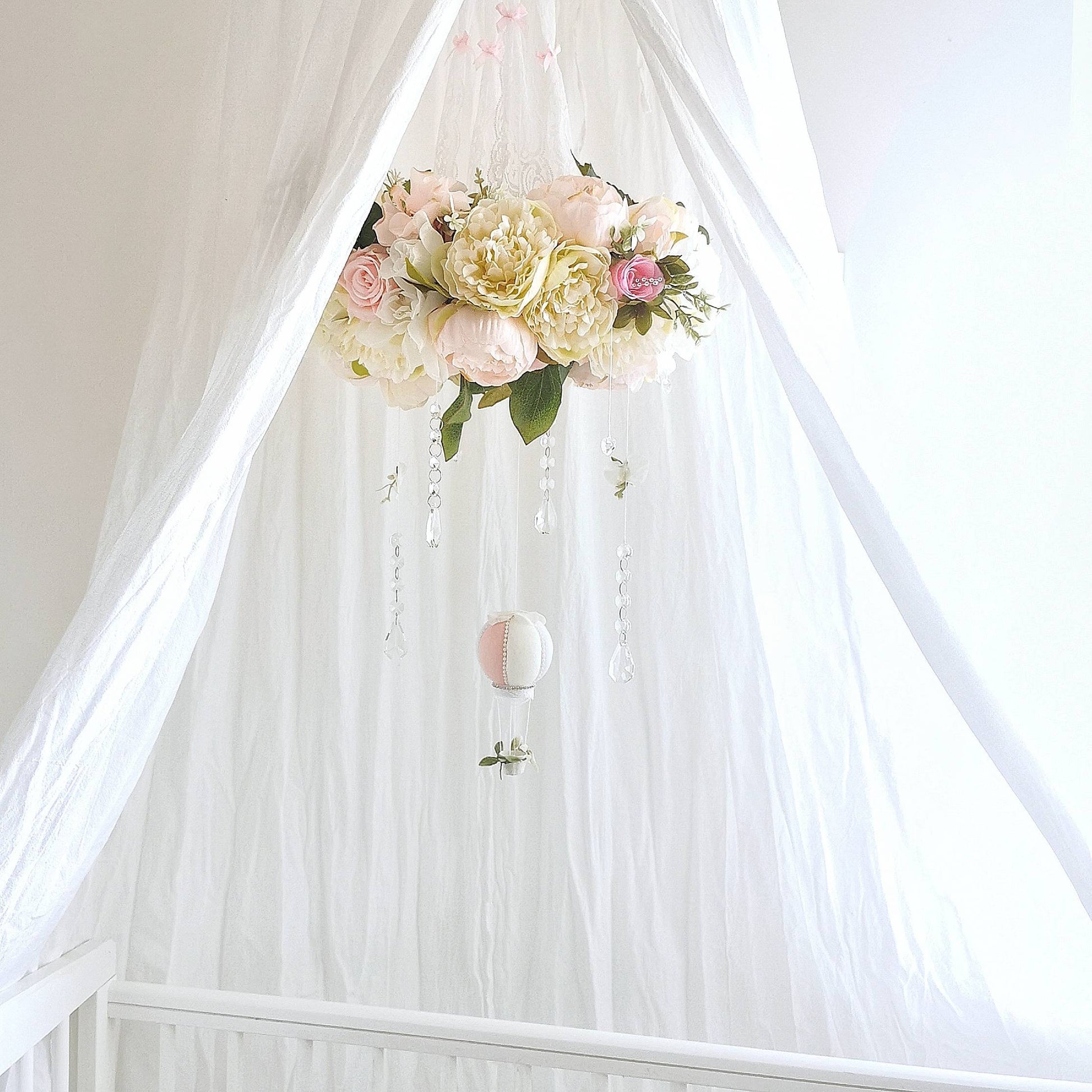 Baby mobile with a garden-style floral ring in blush and cream tones, accented by crystals and leaves.