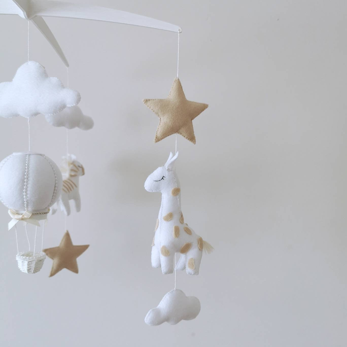 This darling felt giraffe, with its peaceful gaze and warm neutral tones, floats among clouds, adding timeless charm to a luxury safari-themed baby mobile.

