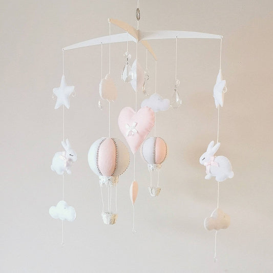 Handcrafted baby mobile in soft pink tones with hot air balloon, bunny, hearts, clouds, and crystal drops.

