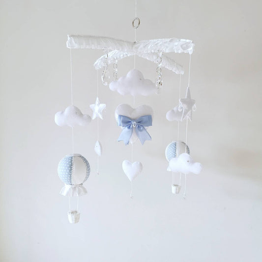 Handmade baby mobile in soft white and blue with clouds, stars, balloon, and teddy bear hanging from a cross hanger.

