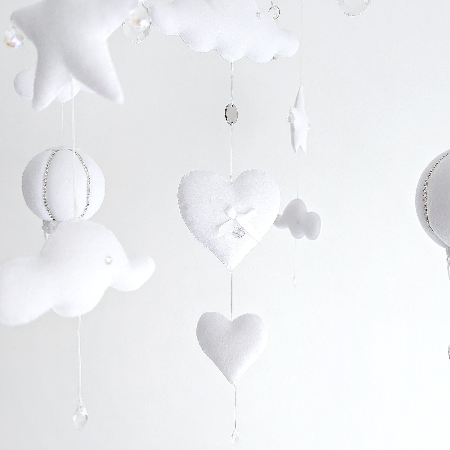 Handmade baby mobile with floating hot air balloons and cloud elements, creating a peaceful, airy scene above the cot.

