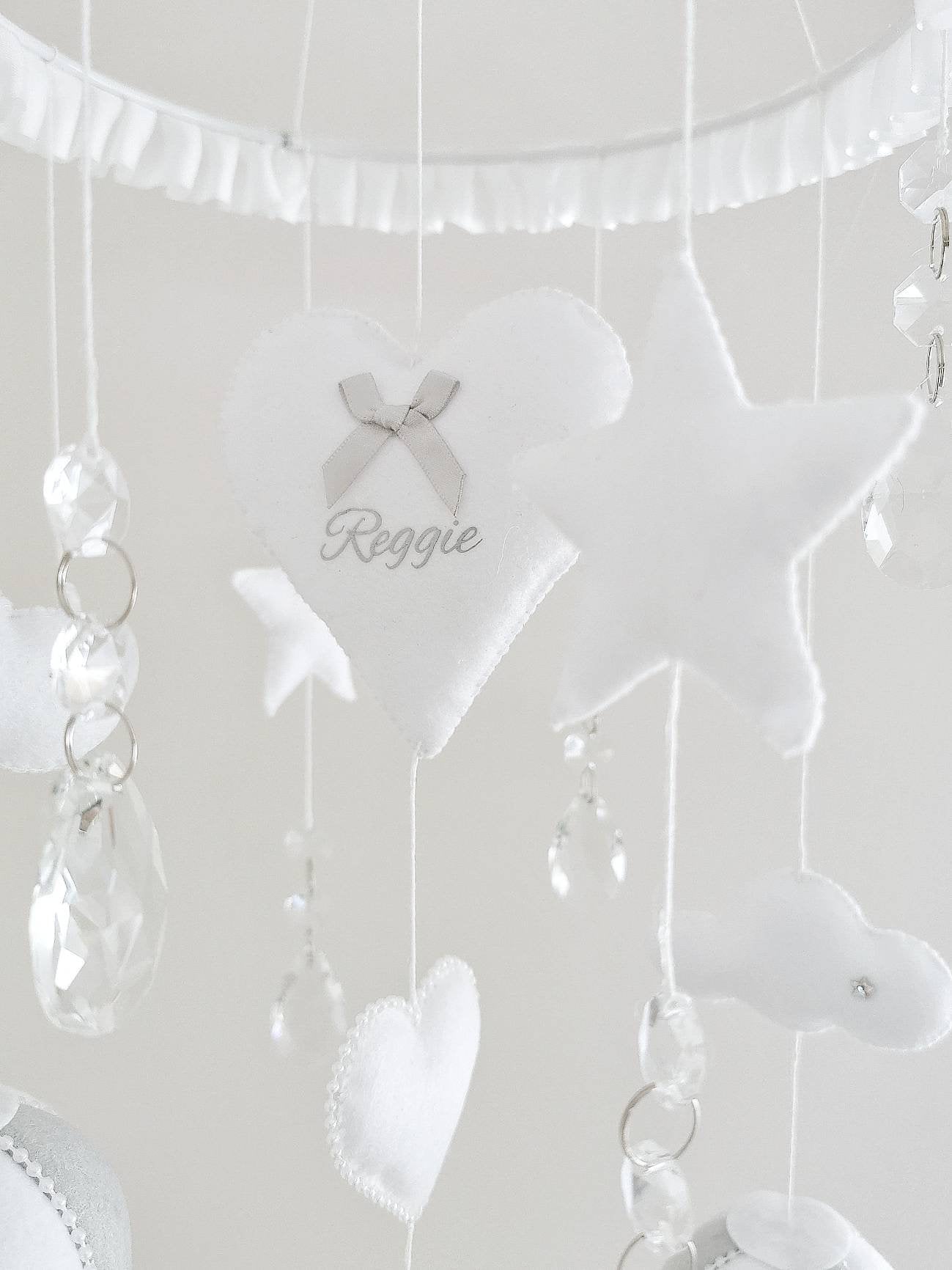 Heirloom baby mobile featuring white balloons, crystal drops, and a personalised heart with the name Reggie.

