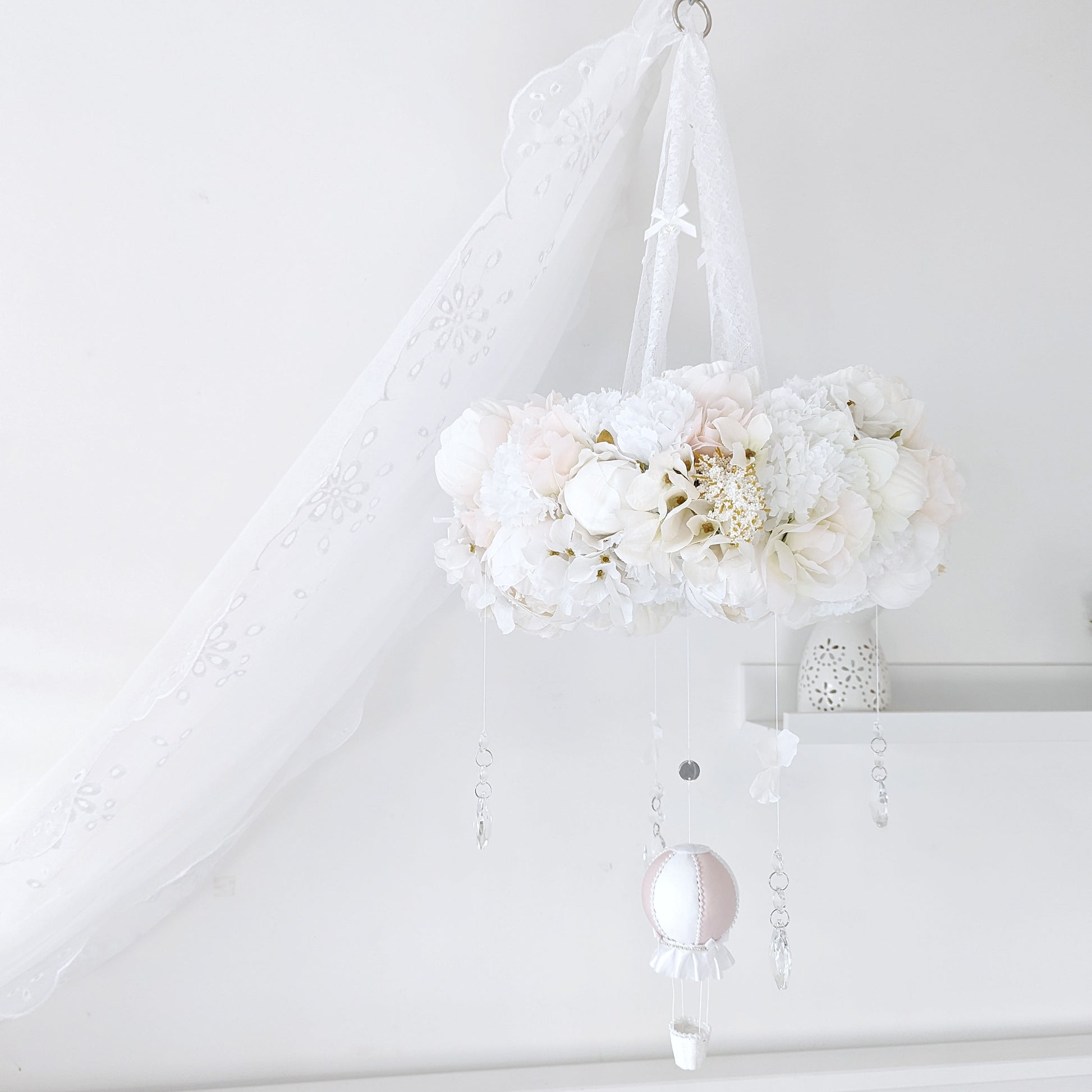 Elegant baby mobile with a lush floral wreath and a single blush pink hot air balloon, styled in a soft white nursery.
