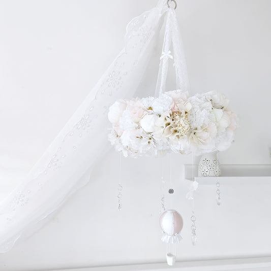 Elegant baby mobile with a lush floral wreath and a single blush pink hot air balloon, styled in a soft white nursery.