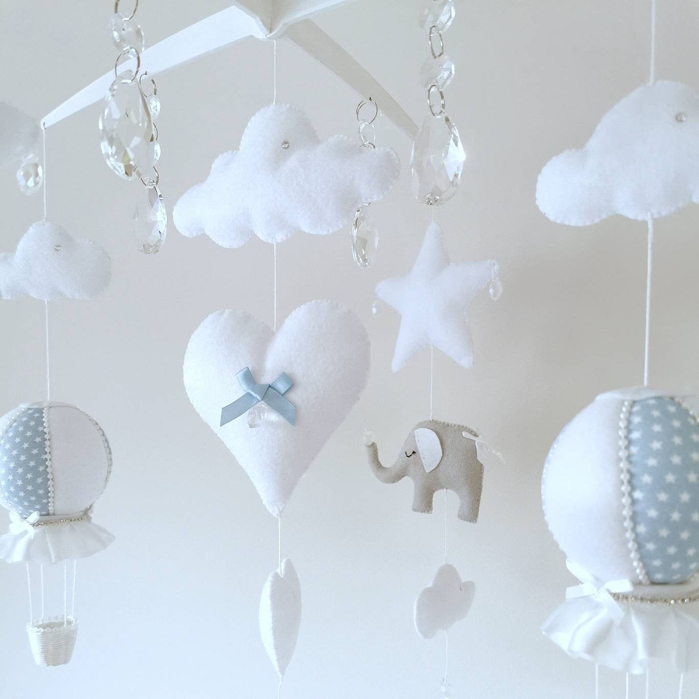 dainty star pale blue and white hot air balloons and soft felt pieces hang gently from this handcrafted nursery mobile with luxury details. Crystal drops and a signature wooden cross hanger

