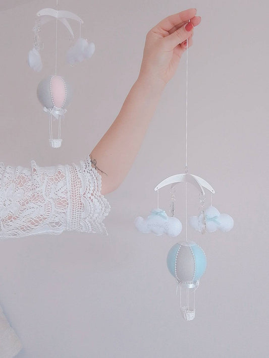 Mini hot air balloon baby mobile in soft blue and ivory with hanging clouds, shown held in hand, perfect for moses basket or bassinet. Baby shower, christening or birth gift

