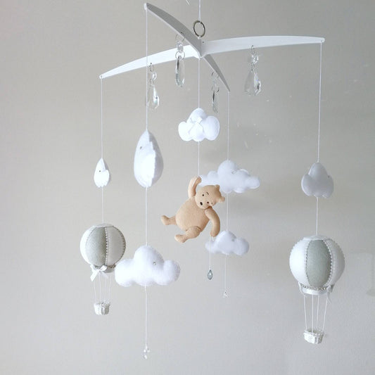 Handmade baby mobile with a soft honey bear  floating among clouds and hot air balloons bringing a warm storybook charm to the nursery

