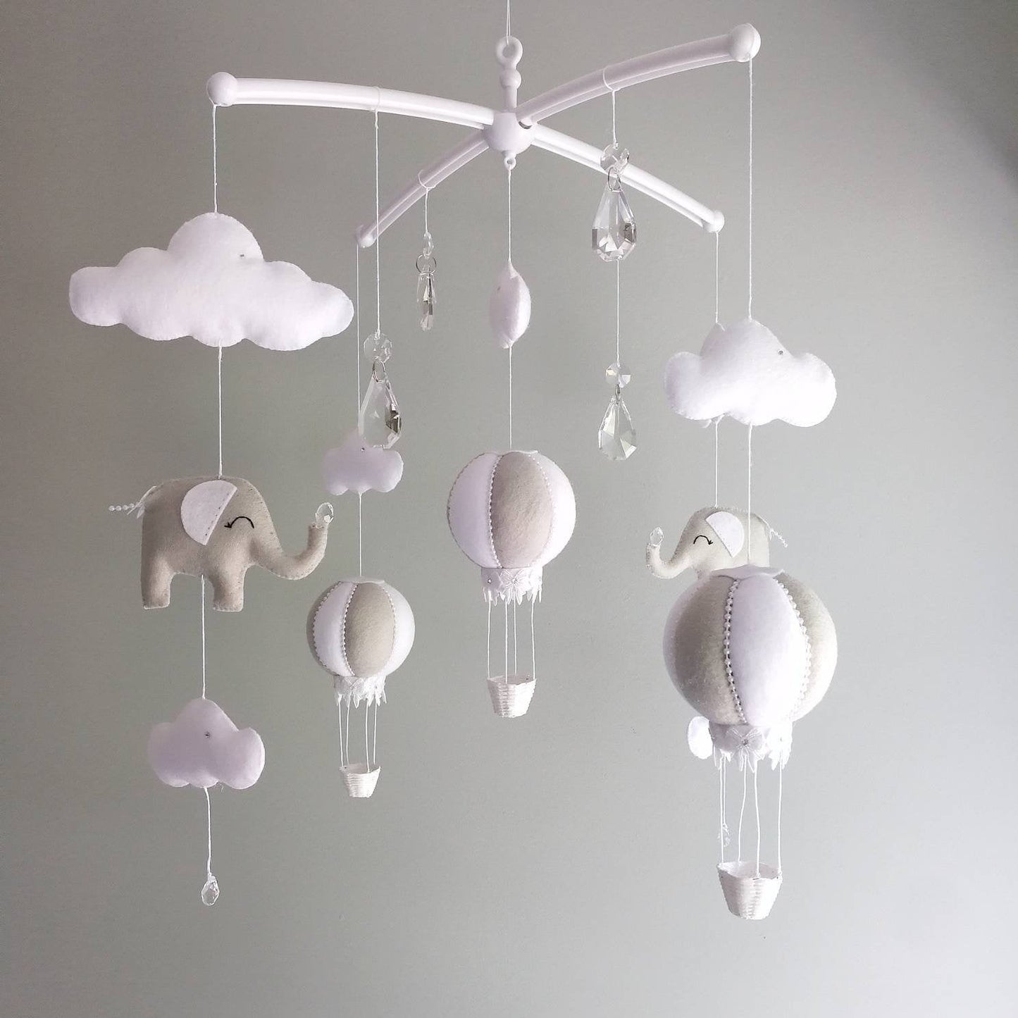 A gentle mix of hot air balloons, elephants, and cloud shapes swaying softly to create a calm and elegant nursery atmosphere.